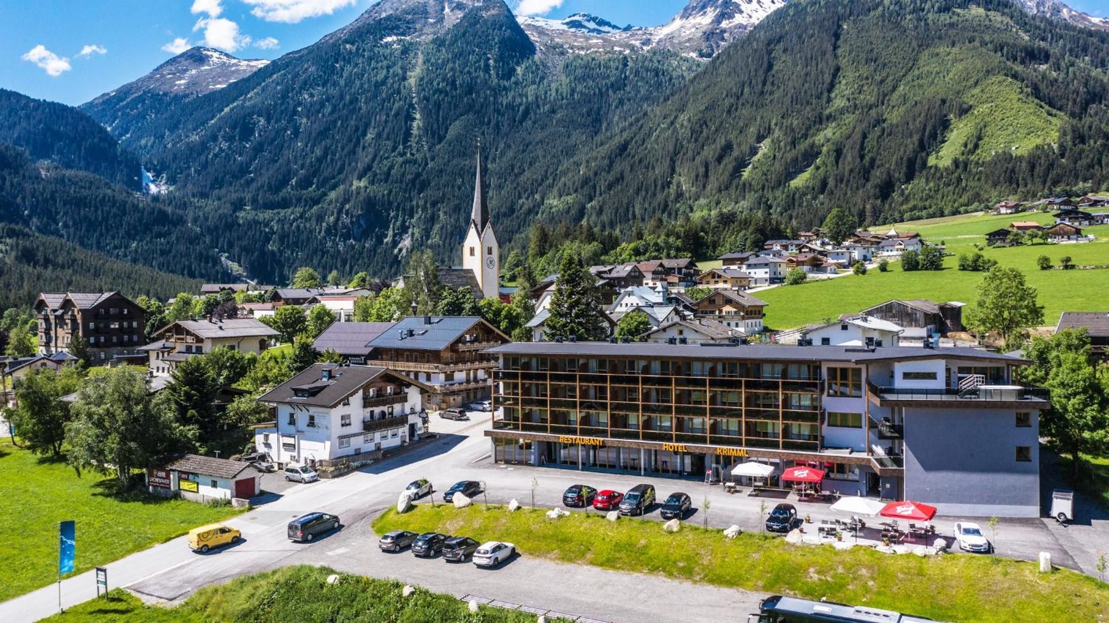 Een stad aan de voet van de bergen, met een opvallend hotel, een kerk en een parkeerplaats met auto's.