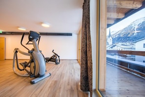 Una habitación con cinta de correr y bicicleta estática, suelo de madera, un ventanal con vistas a una montaña nevada y techo de madera.