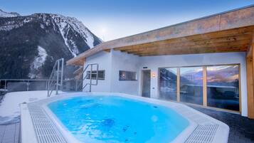 Een hottub met uitzicht op de bergen, een houten terras en een glazen deur naar een kamer.