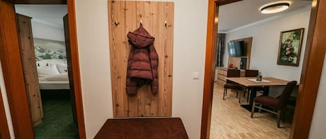 A room with a wooden wall, a coat hanging, a small table with chairs, and a television.