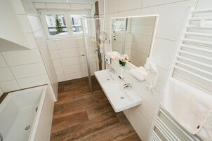 A bathroom with a wooden floor, a white sink, a mirror, and a shower.