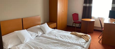 A hotel room with a double bed, a wardrobe, a desk with a chair, and a television.