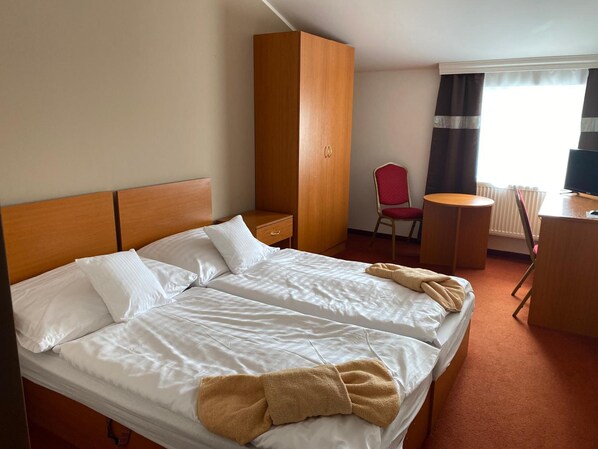A hotel room with a double bed, a wardrobe, a desk with a chair, and a television.