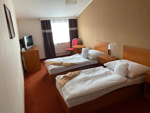 A hotel room with two beds, a desk with a television, a chair, and a window with curtains.