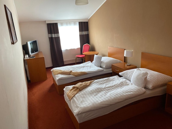 A hotel room with two beds, a desk with a television, a chair, and a window with curtains.