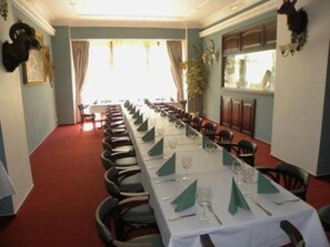 A long dining table set for a meal with chairs on both sides, a red carpet, and a view of the outdoors through a window.