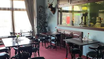 A dining area with multiple tables and chairs, a mounted deer head on the wall, and a window with curtains.