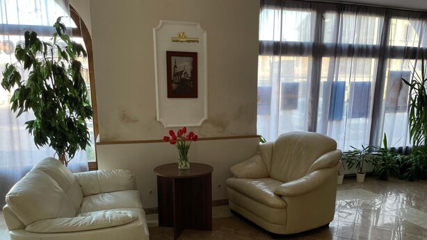 A room with two white leather sofas, a small round table with a vase of red flowers, and a framed picture on the wall. - Hotel Aernvo Orel Oatec (Zatec)