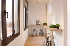 Un pasillo estrecho con suelo de madera, un ventanal de marco oscuro y un estante con plantas.