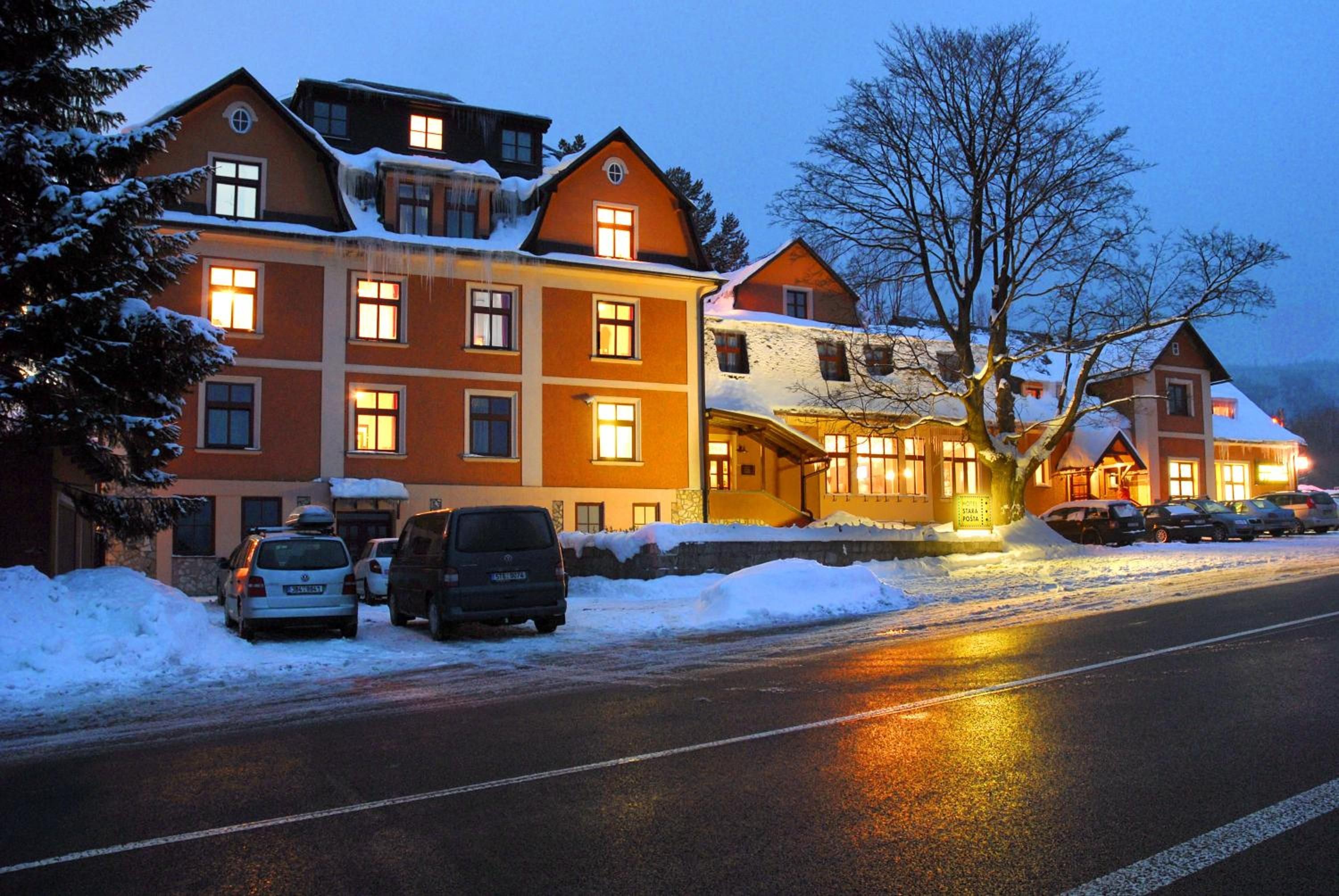 Ein Hotel mit mehreren Etagen, schneebedeckten Dächern und einem Parkplatz mit Autos.