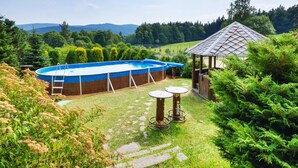 An outdoor swimming pool with a wooden deck and a gazebo in a lush garden setting. - Hotel Stara Posta (Bela pod Pradedem)