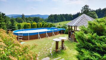 An outdoor swimming pool with a wooden deck and a gazebo in a lush garden setting.