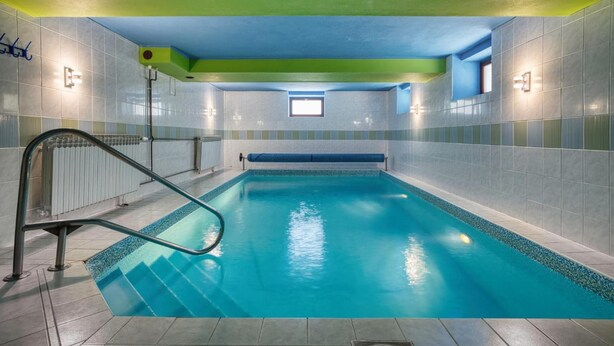 An indoor swimming pool with clear blue water, surrounded by tiled walls and a green ceiling. - Hotel Stara Posta (Bela pod Pradedem)