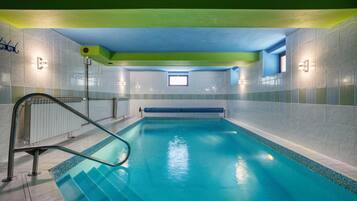An indoor swimming pool with clear blue water, surrounded by tiled walls and a green ceiling.