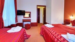 A hotel room with two beds, a TV, a desk with a mirror, and a bathroom door. - Hotel Stara Posta (Bela pod Pradedem)