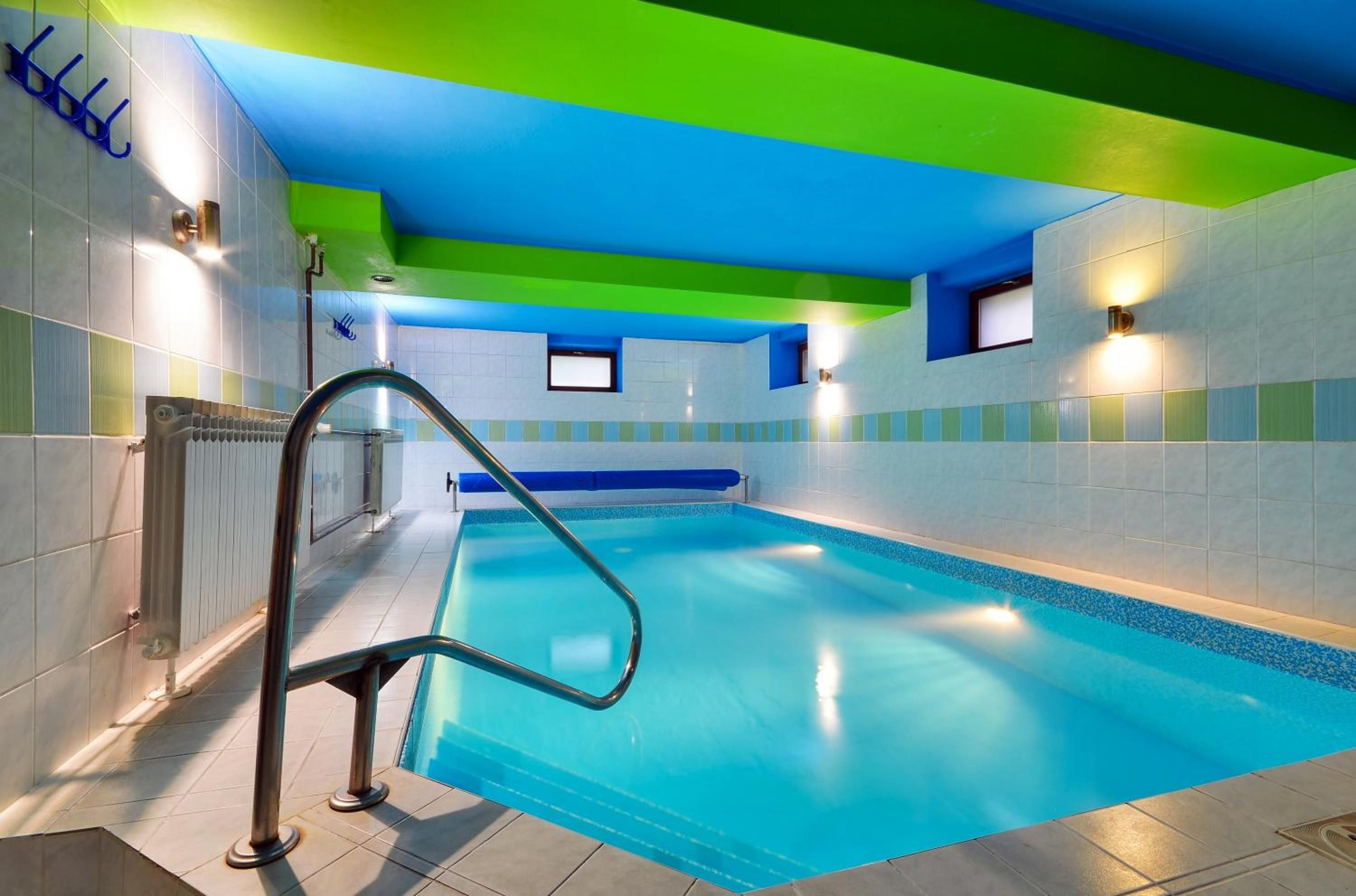 A swimming pool with a blue interior, surrounded by walls with a green and blue color scheme, and a metal ladder leading into the pool.