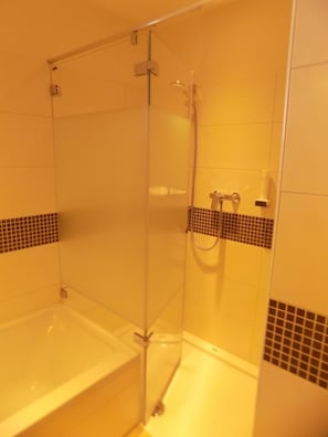 A bathroom with a glass-enclosed shower, a bathtub, and tiled walls.