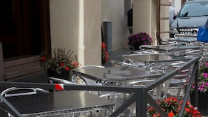 Espace extérieur aménagé avec des tables et des chaises en métal, des plantes en pot ornées de fleurs rouges et une voiture garée à proximité.