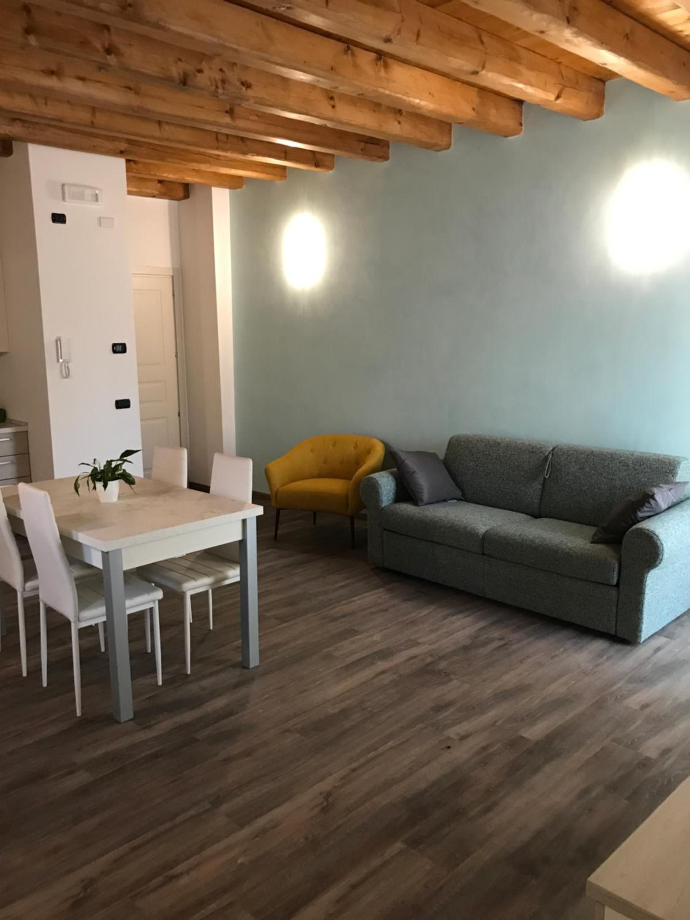 A modern living room with a wooden ceiling, a grey sofa, a yellow armchair, and a dining table with chairs.