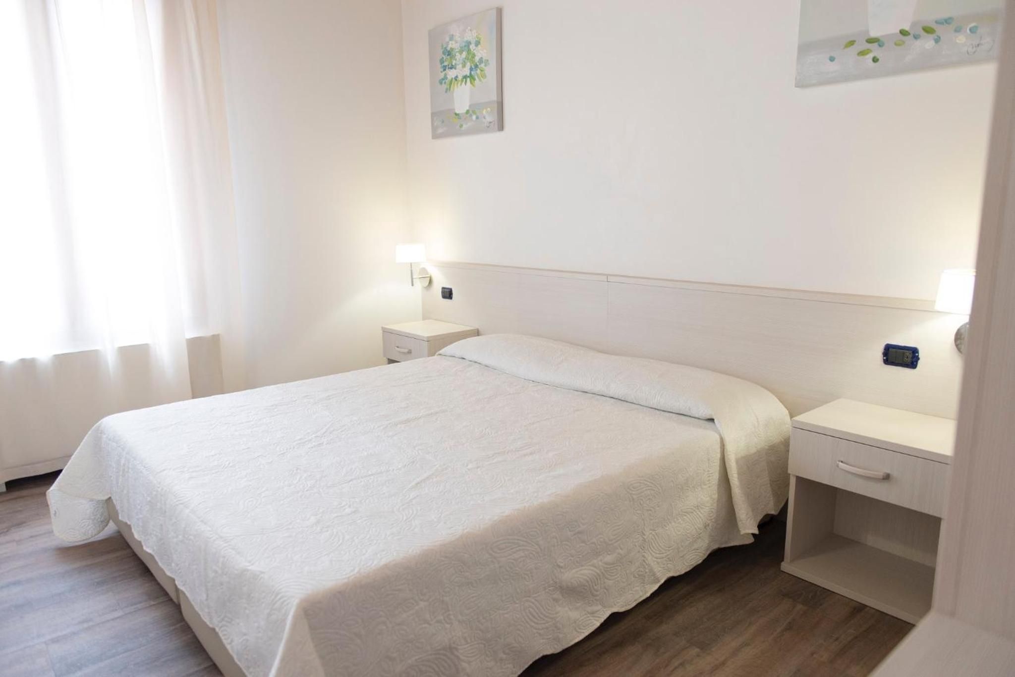 Una camera d'albergo con un letto, comodini, una lampada a parete e tavolini di fianco al letto.