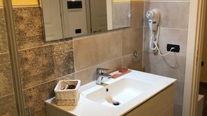Une salle de bain avec un lavabo blanc, un miroir, un sèche-cheveux et un porte-serviettes.