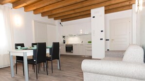 Une cuisine moderne avec des meubles blancs, un coin repas comprenant une table et des chaises, et un canapé gris.