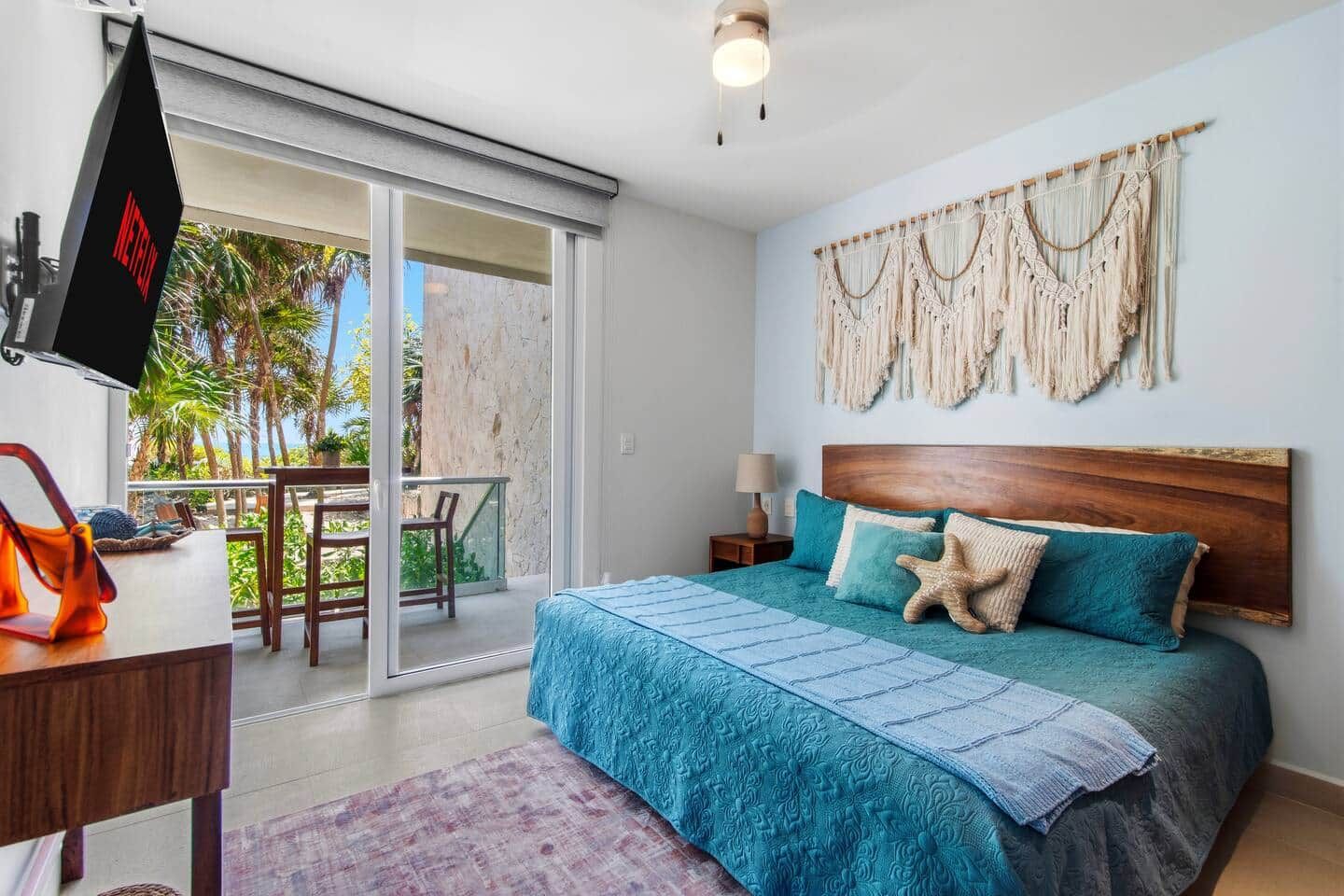 A bedroom with a bed, a TV, a desk, and a balcony with a table and chairs.