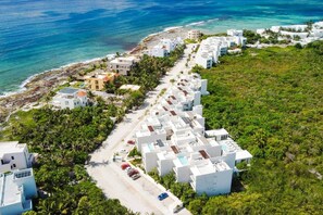 Zona residencial costera con edificios blancos modernos, una playa y abundante vegetación.