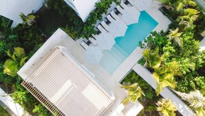 Vue aérienne d’un hôtel moderne doté d’une piscine, entouré d’une végétation luxuriante et de palmiers.