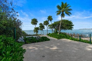 Un camino de concreto que lleva a una playa con palmeras y una valla.