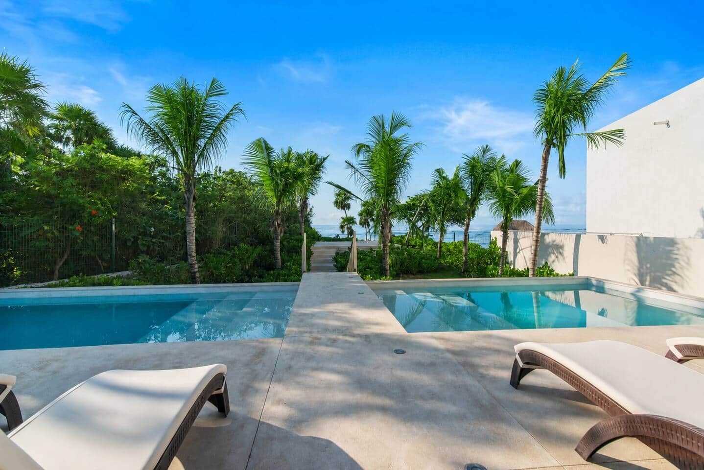 Ein Poolbereich mit Liegestühlen, Palmen und freiem Blick auf das Meer.