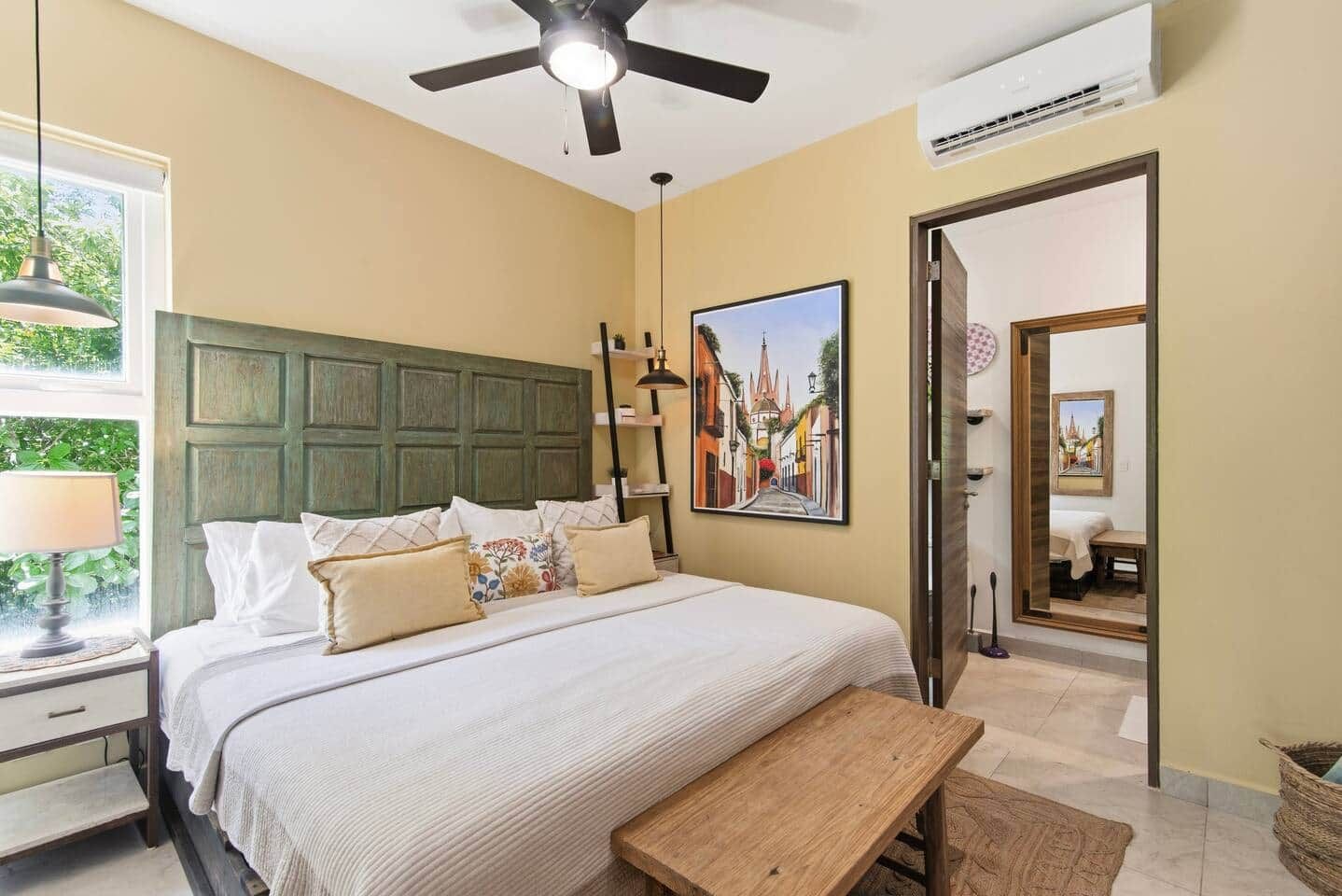 Een slaapkamer met een bed, nachtkastje, lamp, plafondventilator, airconditioning en een schilderij aan de muur.