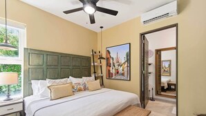 A bedroom with a bed, bedside table, lamp, ceiling fan, air conditioning unit, and a painting on the wall. - Akumal Bosque | 8 Min Walk To Beach | Rooftop Pool (Grand Sirenis)