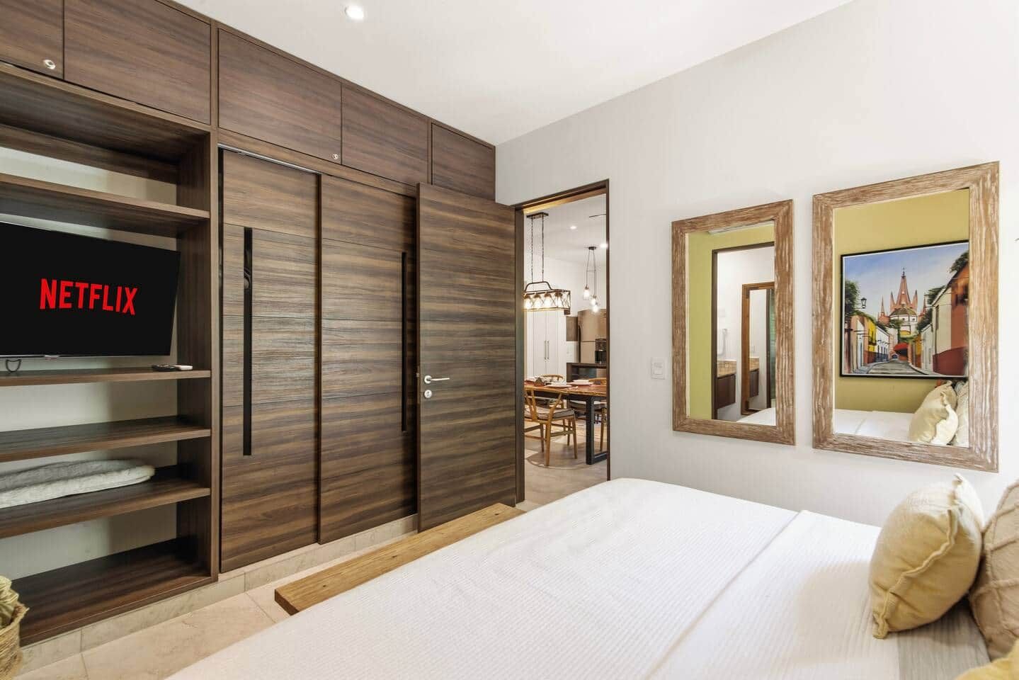 A bedroom with a bed, a wardrobe, a television displaying 'NETFLIX', and two framed pictures on the wall.