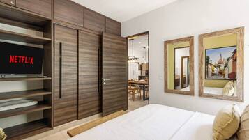 A bedroom with a bed, a wardrobe, a television displaying 'NETFLIX', and two framed pictures on the wall.