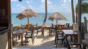 An outdoor seating area with tables and chairs, thatched umbrellas, and a view of the ocean. - Akumal Bosque | 8 Min Walk To Beach | Rooftop Pool (Grand Sirenis)
