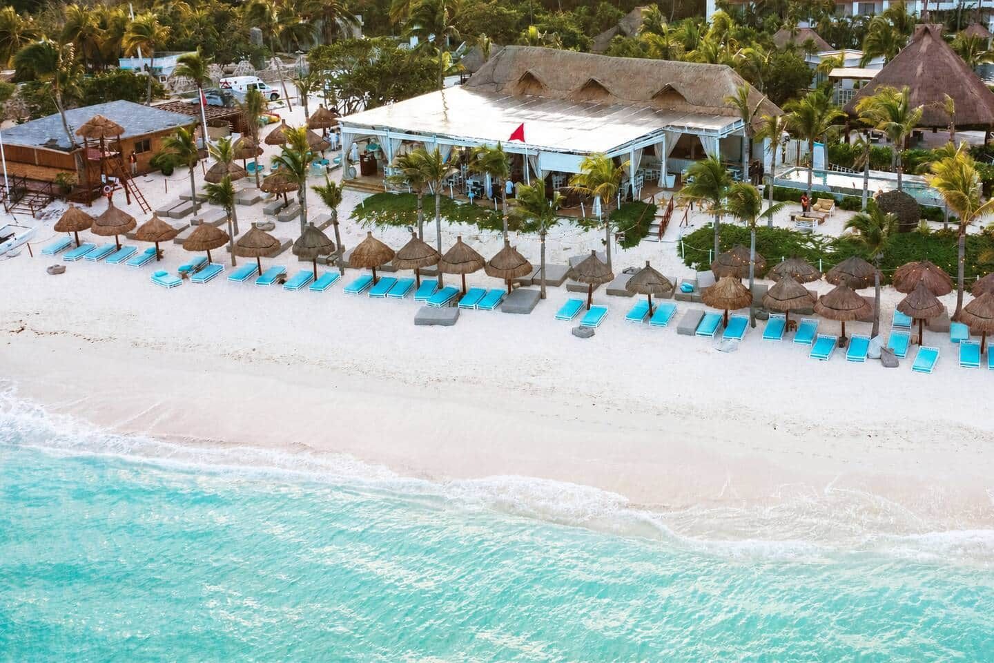 A beachside resort with a pool, lounge chairs, and thatched umbrellas.