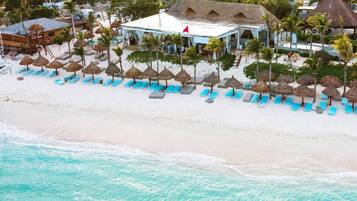 A beachside resort with a pool, lounge chairs, and thatched umbrellas.