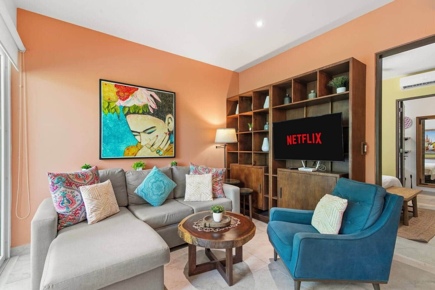 A living room with a sofa, armchair, coffee table, and a TV displaying 'NETFLIX'.