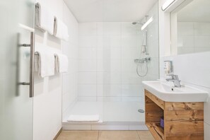 Un baño moderno con cabina de ducha de vidrio, tocador de madera y toallero de pared.