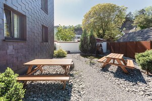 Un patio con dos mesas de picnic de madera, un sendero de grava y un edificio de ladrillo con ventanas.