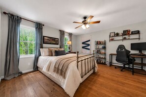 A bedroom with a bed, a desk with a computer, a bookshelf, and a ceiling fan.