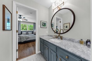 A bathroom with a large mirror, marble countertop, and a bed visible through an open door. - Private 7-Acre Luxury Knoxville Retreat. Sleeps 14. Theater + Game Room (Knoxville)