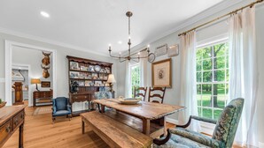 Una sala da pranzo con un tavolo e sedie in legno, un lampadario e una libreria piena di cornici e oggetti decorativi.