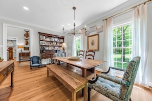 A dining room with a wooden table and chairs, a chandelier, and a bookshelf filled with framed photos and decorative items. - Private 7-Acre Luxury Knoxville Retreat. Sleeps 14. Theater + Game Room (Knoxville)