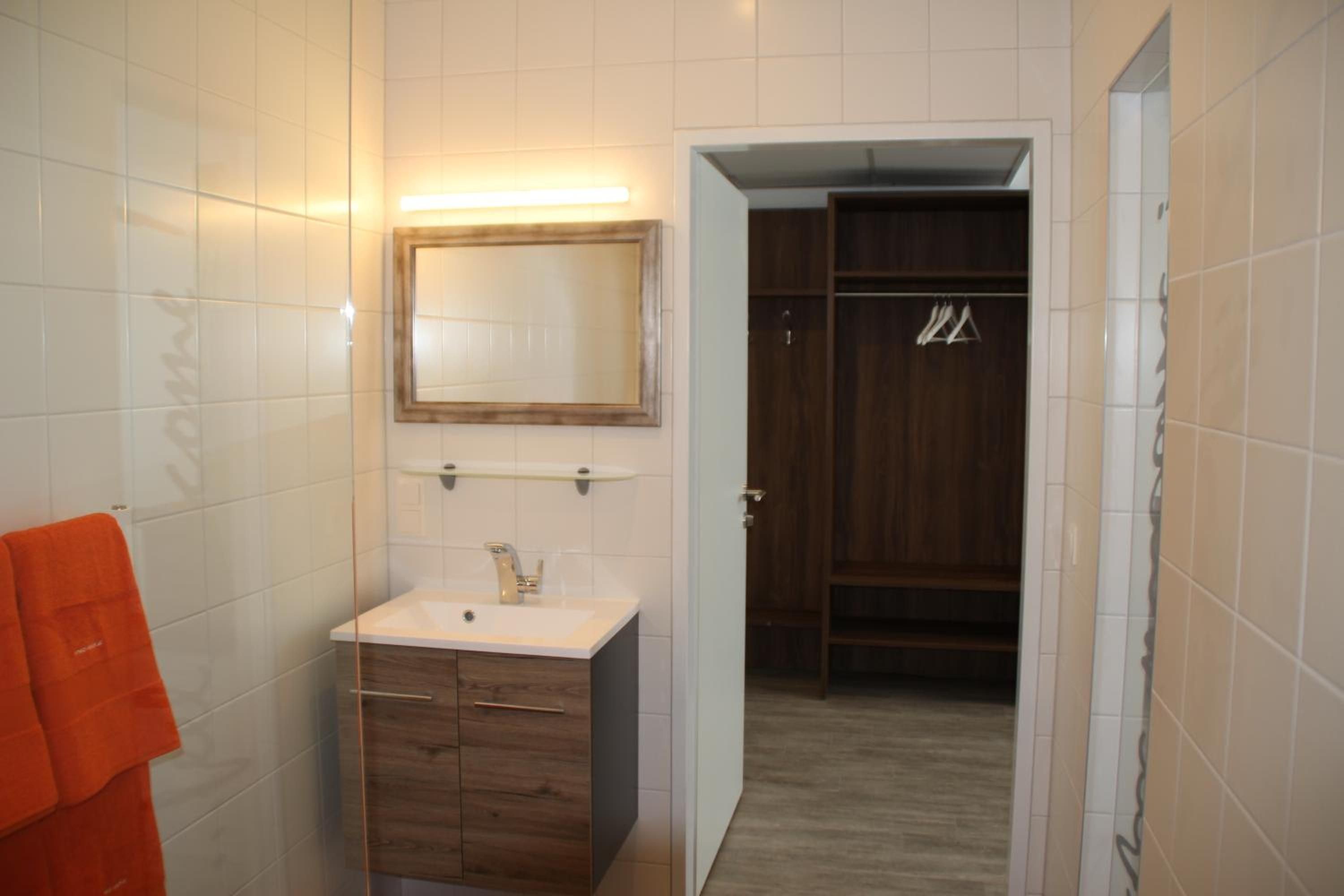 A bathroom with white tiles, a wooden vanity, a mirror, and a towel rack.