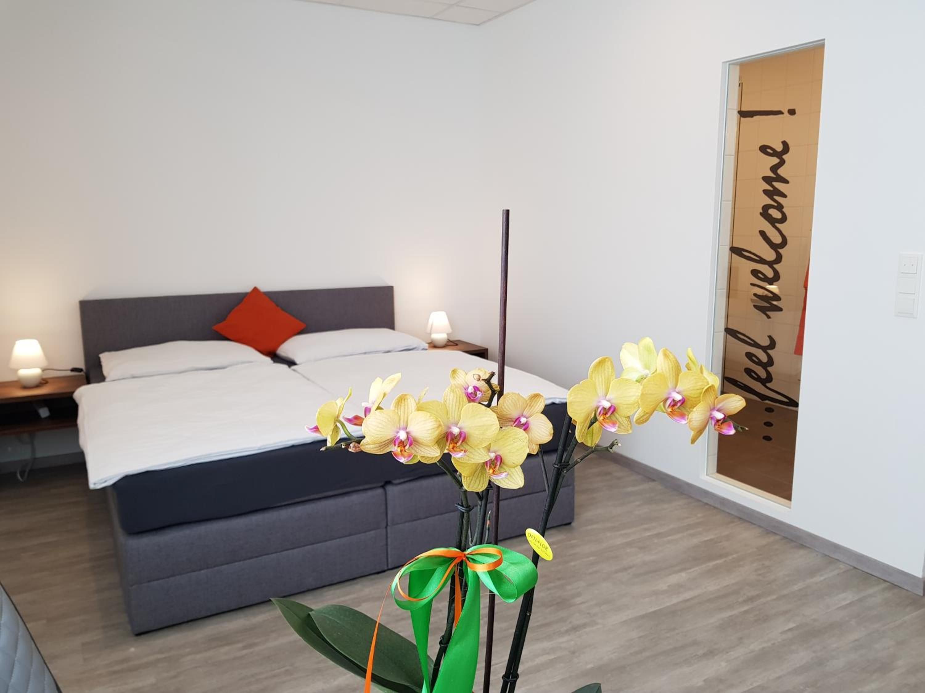 A hotel room with a bed, a nightstand, a lamp, and a decorative orchid arrangement.