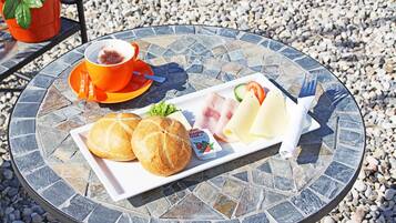 A round table with a mosaic tabletop, a plate with bread, cheese, and a small container of yogurt, a cup with a spoon, and a plant in a red pot.