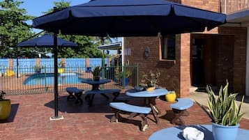 Een terras buiten met tafels en stoelen, een zwembad en een bakstenen gebouw op de achtergrond.