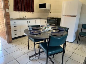Uma cozinha com mesa de jantar, cadeiras, micro-ondas, geladeira e pia.